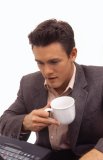 Portrait of an attractive Caucasian male drinking from a mug and using a laptop computer.