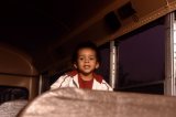A young boy peaking over a seat inside a school bus.