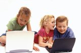 Three young kids play on laptops.