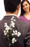A man holds a flower behind his back to surprise his girlfriend.