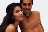 Portrait of a man holding a strawberry by the stem in his mouth while a woman admires.