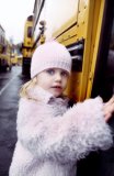 A young girl poses while getting inside a schoolbus.