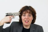 Woman in suit with a gun pointing gun at her head.