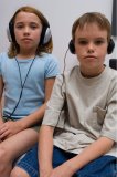 Portrait of two young kids sitting on a bed while listening to head phones.