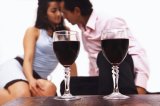 Portrait of a couple behind two wine glasses kissing.