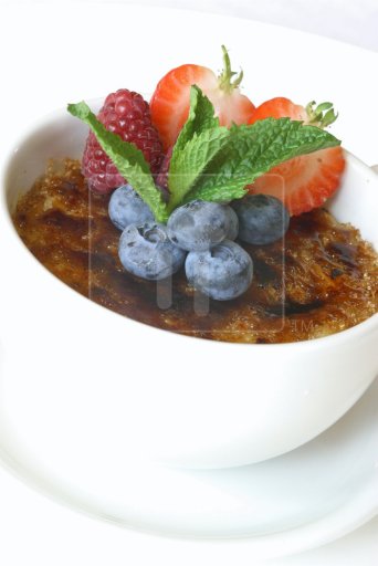 Creme brulee decorated with various fruit.  Served in a white dish.